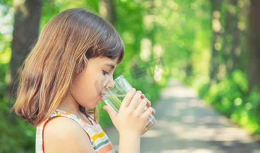 一个孩子在大自然中从玻璃杯里喝水。