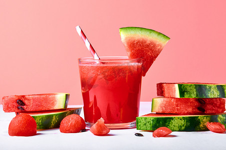 夏天西瓜背景摄影照片_特写新鲜西瓜汁或冰沙在玻璃杯与西瓜片粉红色背景。