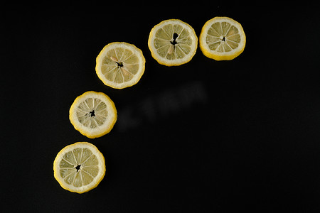 上半圆半圆摄影照片_五片柠檬片在黑色背景上排成半圆，隔离