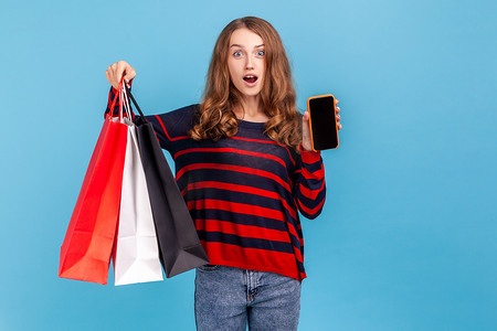 智能服务摄影照片_女人站着拿着手机，手机上显示着空的促销品和购物袋。