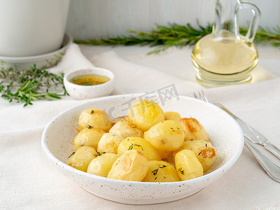 在烤箱中烘烤，香料围绕整个马铃薯块茎，放在白色纺织背景的盘子里，金色的外壳，侧视图