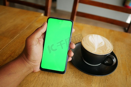 手机花屏摄影照片_拿着咖啡的CPU并使用带绿屏的智能手机