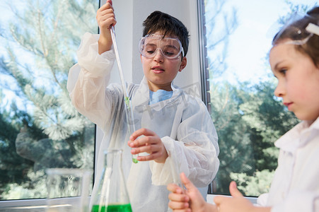 英俊的学童穿着实验室安全服，用吸管将试剂滴入试管，进行化学实验