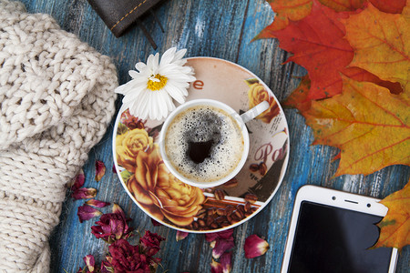 秋季布局、咖啡、橙叶、干玫瑰花瓣、针织毛衣、笔记本和笔、智能手机。