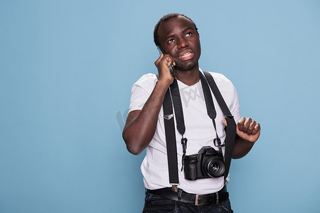 快乐的摄影爱好者在蓝色背景上拥有拍照设备时在手机上交谈。