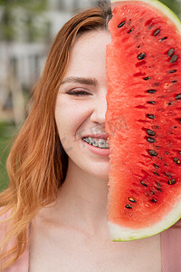夏天，美丽的红发女人戴着牙套微笑，用一片西瓜遮住半张脸