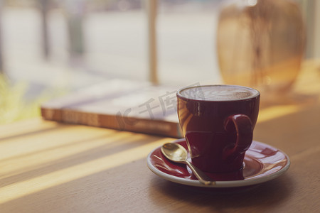 咖啡店木桌上红杯中的热艺术拿铁、卡布奇诺咖啡的特写模糊背景，具有复古风格的散景图像处理