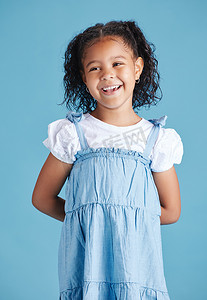 快乐微笑的小女孩双手背后站在蓝色工作室背景下。