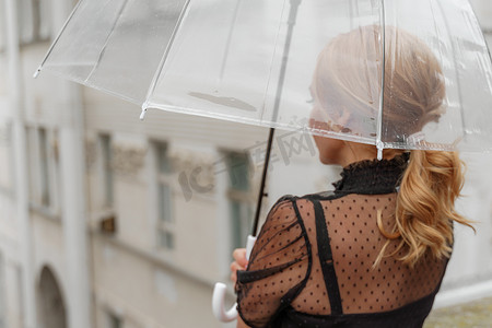 雨中，金发女郎站在透明的雨伞下。