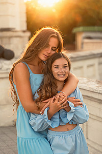 母亲和女儿的肖像，穿着蓝色连衣裙，长发飘逸，在日落的背景下。
