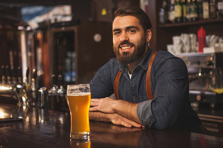 友好的调酒师在他的酒吧提供啤酒时微笑着
