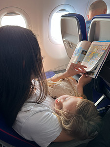 带着熟睡女儿的妈妈坐在飞机座位上看杂志