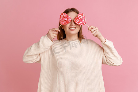微笑的金发女人用美味的心形棒棒糖遮住眼睛，表情俏皮。
