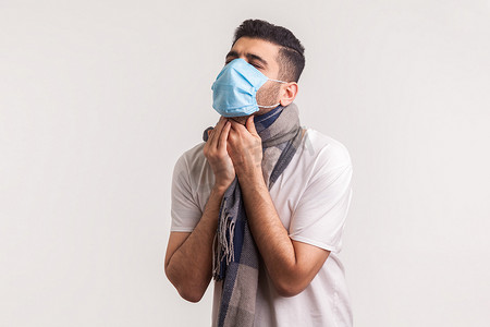 面具摄影照片_戴面具和围巾的男子喉咙痛、咳嗽和窒息，有流感症状