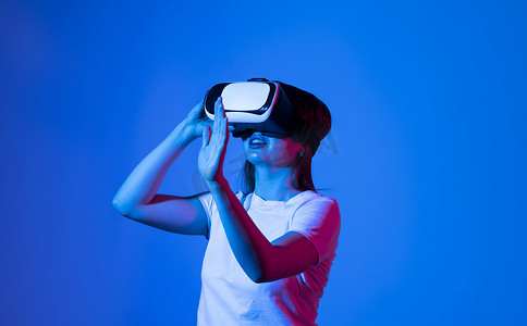 虚拟现实技术摄影照片_美丽的黑发女人在霓虹灯下的 VR 体验中触摸空气。 