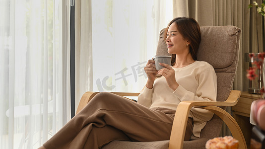 快乐的现代女性穿着温暖的毛衣喝着热咖啡，在秋日享受一缕阳光