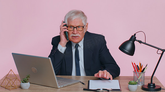 愤怒的高级商人在粉红色办公室打电话惹恼了老板谈论手机争吵