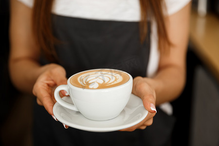 咖啡经营概念-裁剪关闭女性服务咖啡与拿铁艺术，同时站在咖啡店。