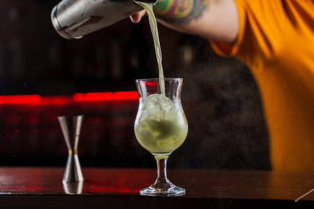 调酒师在酒吧柜台上洒上亮绿色冷鸡尾酒的发光玻璃，并在其上点燃火焰