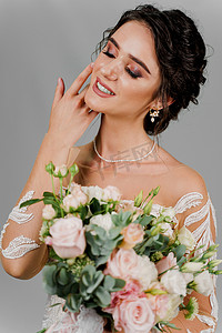 漂亮新娘摄影照片_有婚礼花束的新娘微笑着抚摸她的脸和头发。