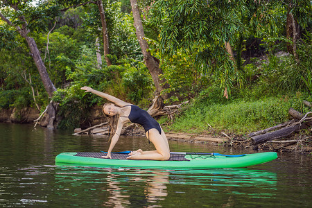 运动型女性在桨板上做瑜伽姿势，在sup板上做瑜伽，锻炼灵活性和伸展肌肉