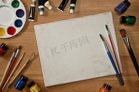 木桌上的空画布画笔、管漆、水彩和调色板。