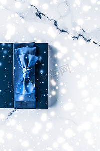 新年新年礼盒摄影照片_冬季节日礼盒，配有蓝色丝绸蝴蝶结、大理石背景上的雪花，作为豪华美容品牌的圣诞和新年礼物，平铺设计