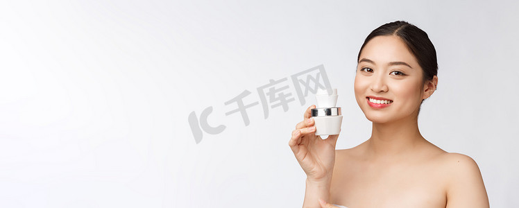 药健康摄影照片_白色孤立背景中美丽的年轻女子拿着化妆品面霜，亚洲人