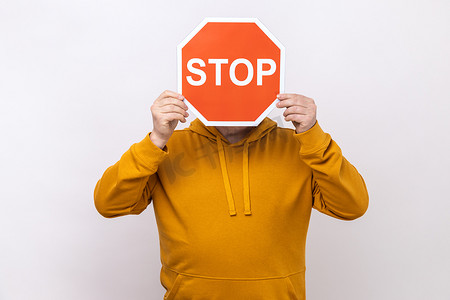 身份不明的人将脸隐藏在“停止”符号后面，红色交通标志警告限制通行。