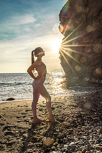 女子体操运动员正在海边日落的海滩上训练。