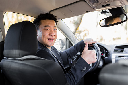 竖大拇指你真棒摄影照片_成功的商人汽车推销员驾驶方向盘的亚洲男性司机