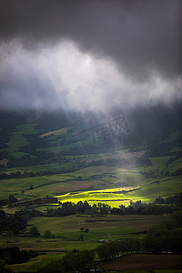 明亮的阳光透过云洞照射到葡萄牙圣米格尔亚速尔群岛山脉的黑暗场景。