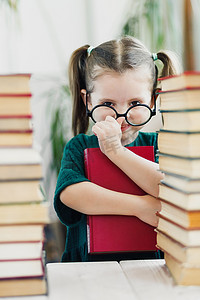 可爱的小女孩穿着绿色的衣服，手里拿着红色的书，鼻子上戴着眼镜。