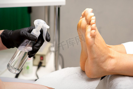 皮肤喷雾摄影照片_修脚师傅在美容院用准备去污的方法对妇女的脚进行消毒。