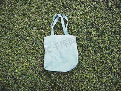 手提袋蓝色摄影照片_绿色灌木树叶背景上的空白蓝色样机亚麻棉手提袋。