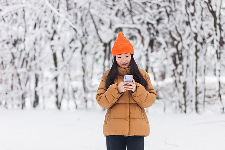 冬天下雪的时候，美丽的亚洲女人在公园里散步，用手机网上购物