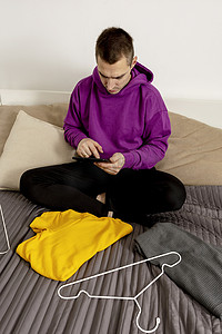 穿着紫色连帽衫的男子使用数字平板电脑拍摄他的旧衣服的照片以在网上出售。