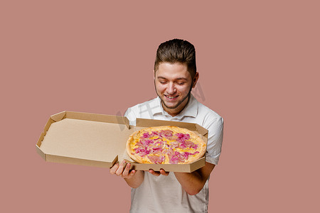 英俊的年轻快乐男人闻着美味的披萨。