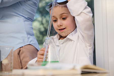 穿着白色实验室外套的聪明白人学龄前女孩学习化学，在学校科学实验室进行实验