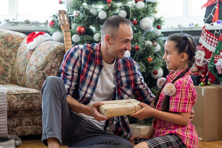 四岁的小女孩和她的爸爸在客厅里装饰着圣诞树和礼品盒，灯光营造出舒适的氛围。
