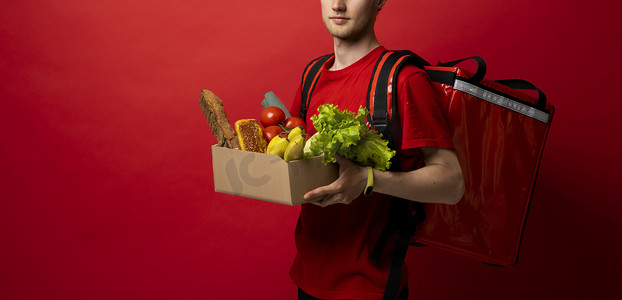 身穿红色制服的送货员携带纸盒的作物图片，纸盒上装有红色背景的食品。