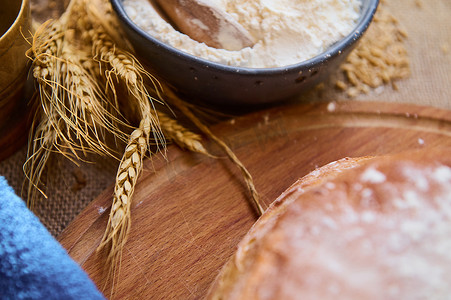 柔和地聚焦在木板上一碗白面粉和新鲜出炉的全麦面包旁边的小麦小穗上