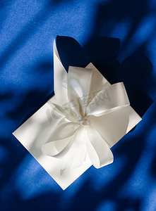 蓝色背景上带丝带和蝴蝶结的豪华假日白色礼盒、豪华婚礼或生日礼物