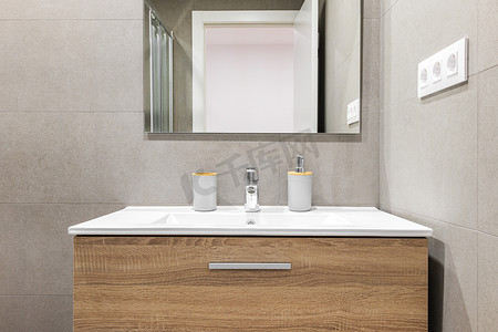 白色水槽特写镜头，配有现代木质底座和翻新浴室中的镜子。