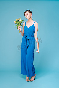 浅色背景中，身穿蓝色连衣裙、手拿鲜花的漂亮女孩