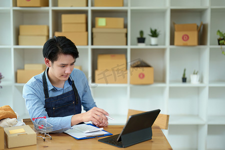 一家小型初创企业和中小企业主的照片，一位亚洲男性企业家检查订单以整理产品，然后将其装入内盒供客户使用
