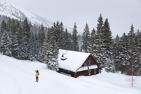 老木屋背景下冬季森林中的摄影师