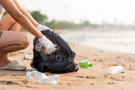 志愿者妇女将塑料瓶放入黑色垃圾塑料袋中清洁海滩
