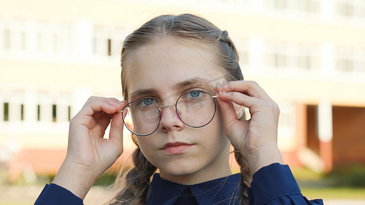 一名戴眼镜的少女在学校门前。