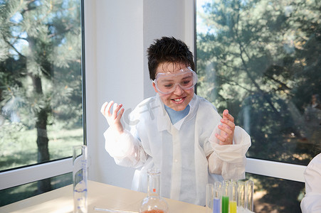 穿着安全眼镜和实验室外套的淘气十几岁的男孩，对化学实验室的科学实验着迷。